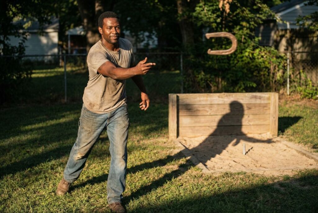 Man pitching horseshoes at regulation distance demonstrating controlled throwing technique influenced by horseshoe weight