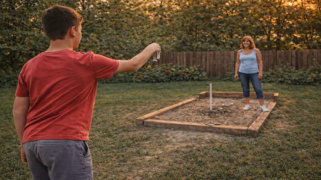 Kid throwing a horseshoe toward the stake while adult watches from the opposite pit in a backyard setting